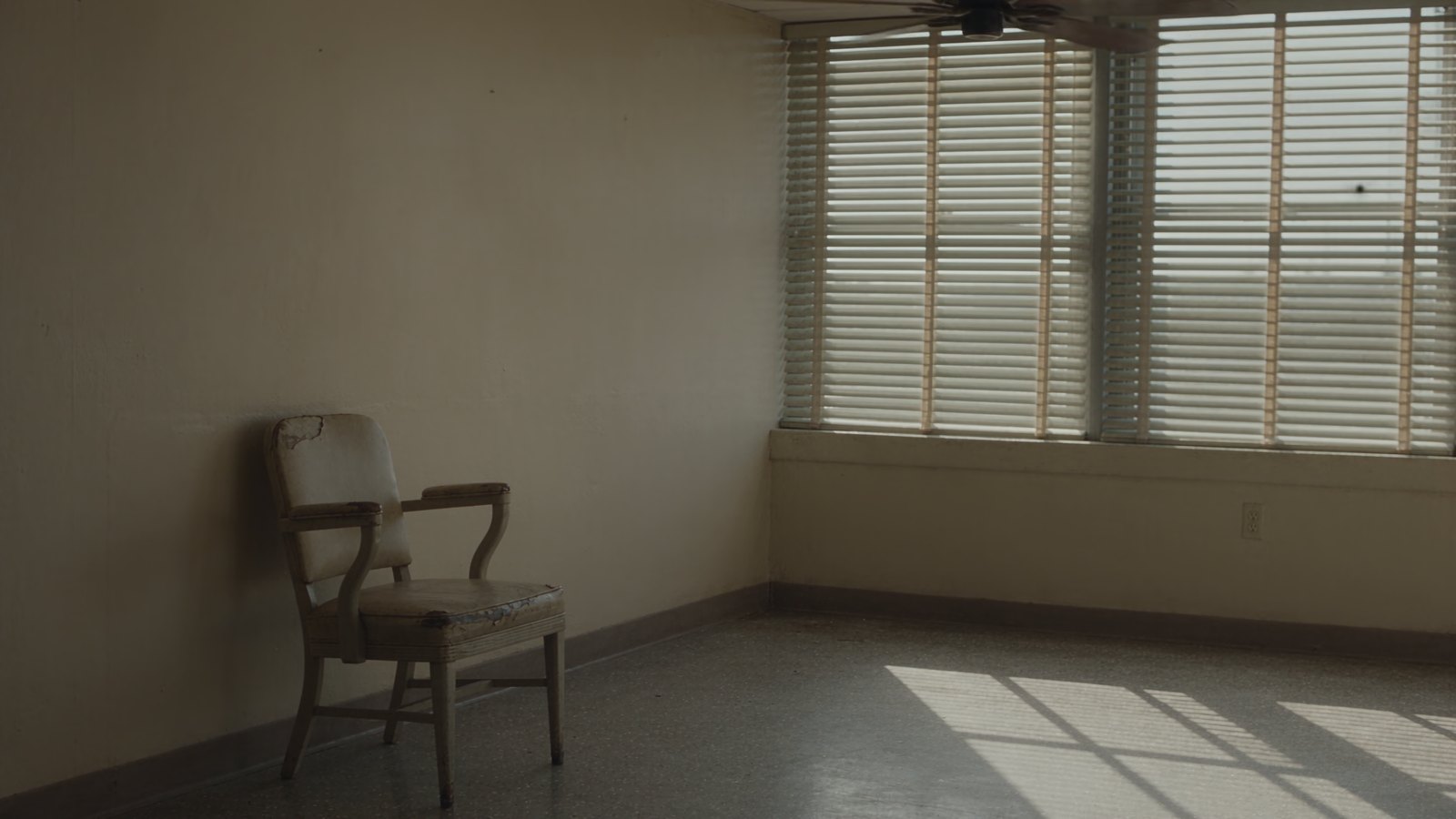 An empty waiting room with one chair under a slowly turning ceiling fan.