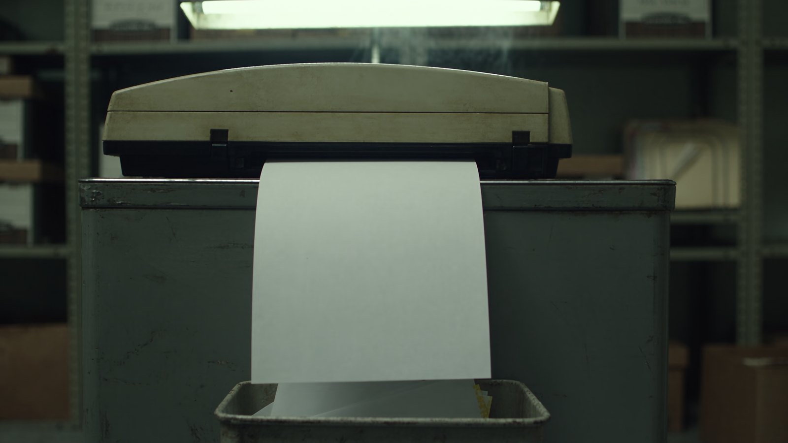 A fax machine feeds a blank page straight down into the wastebasket below it.